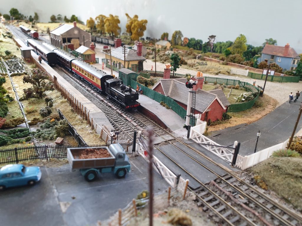 A section of the model railway at the temporary exhibition 'Eynsham's Lost Railway' in December 2023, showing a passenger train, the station, houses vehicles and roads.