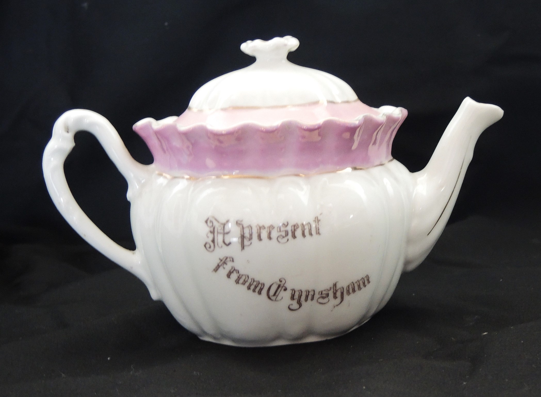 A white and pink fluted teapot with gold lettering that says 'A present from Eynsham'.